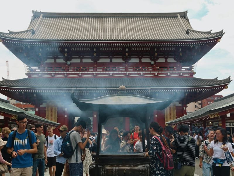 People gathered around incense smoke at the front of Sensoji Temple in Tokyo