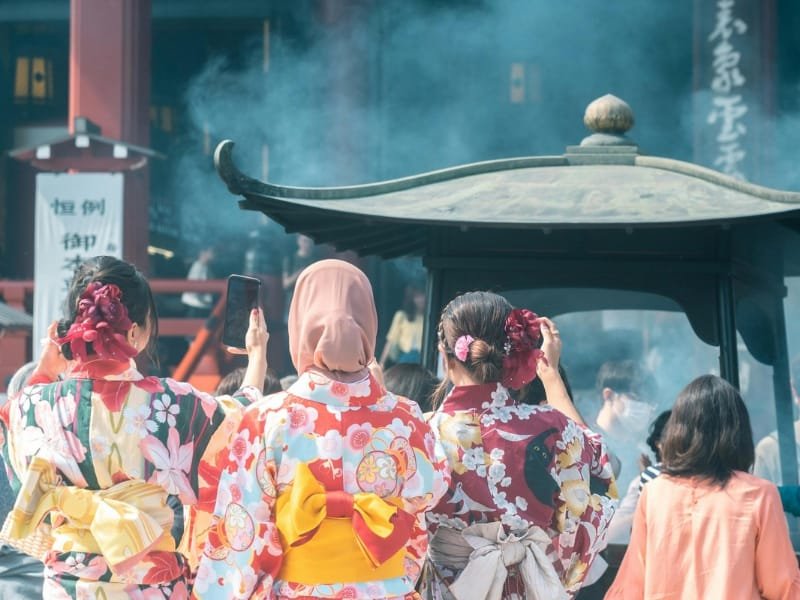 Girls in traditional Japanese dress standing near incense smoke at Sensoji Temple