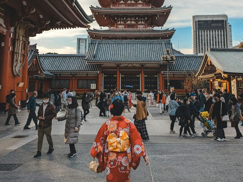 Girl in traditional Japanese dress walking towards Sensoji Temple with a modern bag in hand