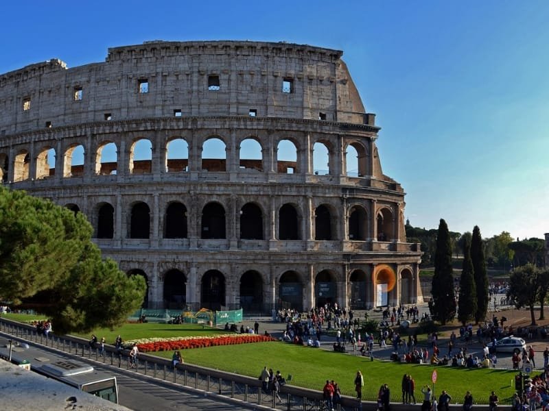 Tourists walking near the Colosseum on a sunny day in Rome.
