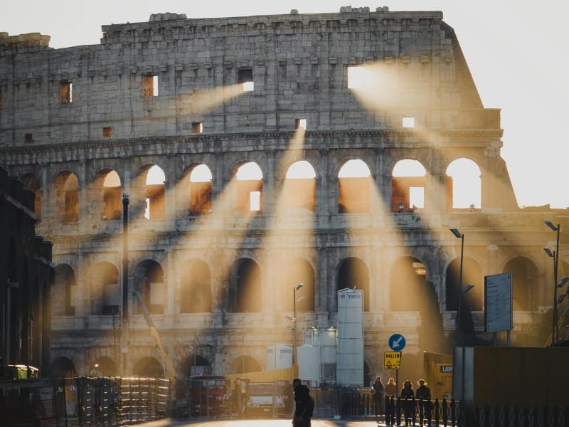 Sunlight streaming through the windows and arches of the Colosseum, casting golden patterns on the ground.