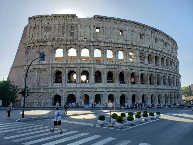 Tourists walking around the Colosseum under bright midday sunlight in Rome.