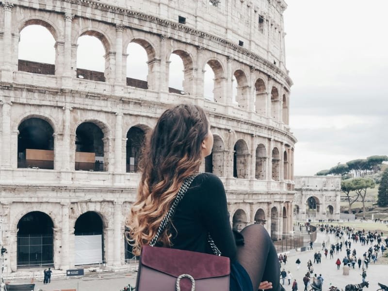Girl sitting on a wall posing in front of the Colosseum in Rome.